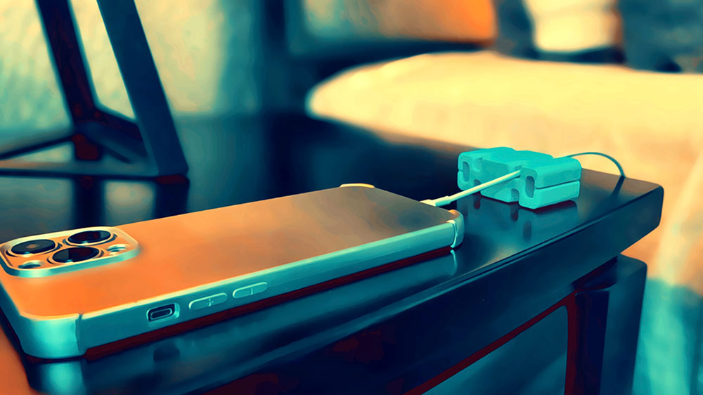 Phone plugged in with cord channeled through CordBrick on a nightstand by a bedside.