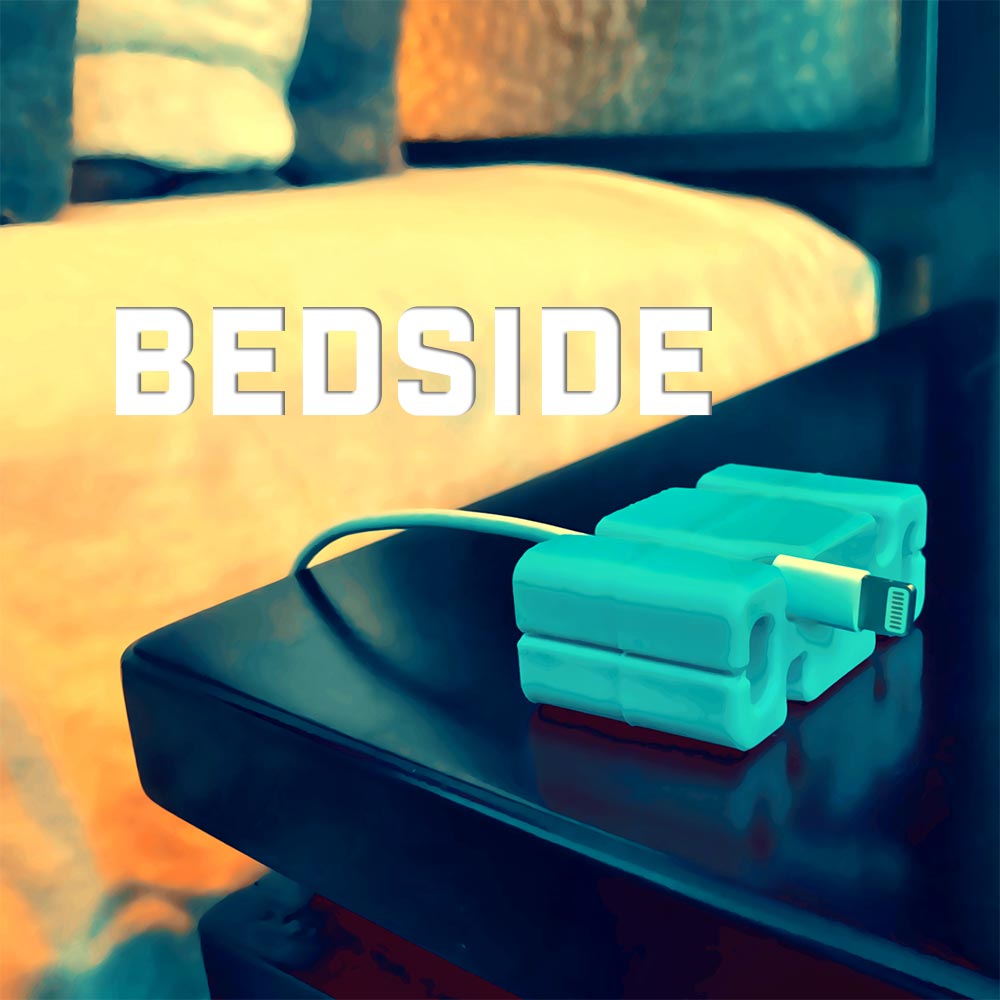 Bedside (in text) aqua CordBrick on black nightstand holding one phone charger cord by a bedside.