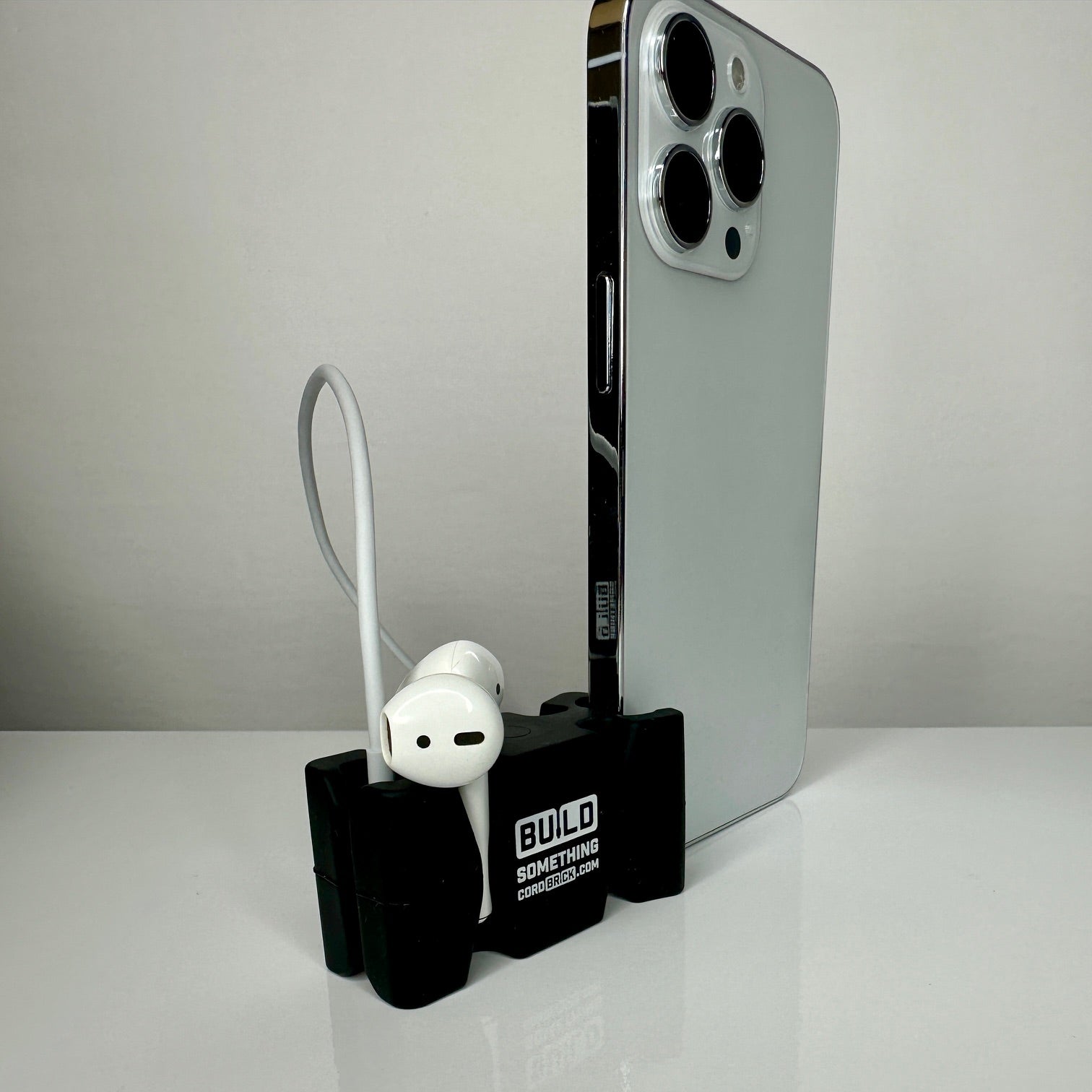 Black promo CordBrick stand phone and holds ear buds on a white desktop